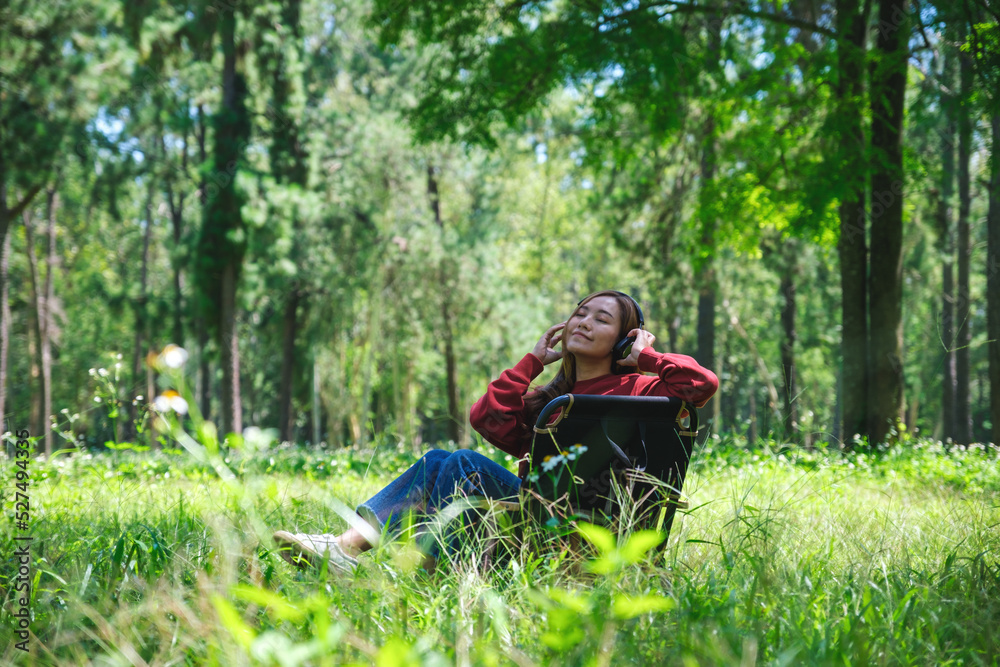 Portrait of a beautiful young asian woman enjoy listening to music with headphone while sitting on a camping chair in the park Portrait of a beautiful young asian woman enjoy listening to music with headphone while sitting on a camping chair in the park