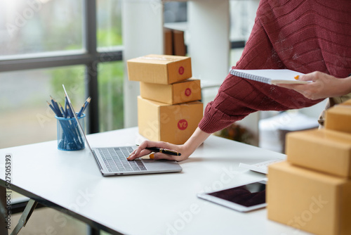 Close-up of a young woman who owns an online packaging business for a customer. Check the customer address list to properly pack and ship to the customer. © amnaj