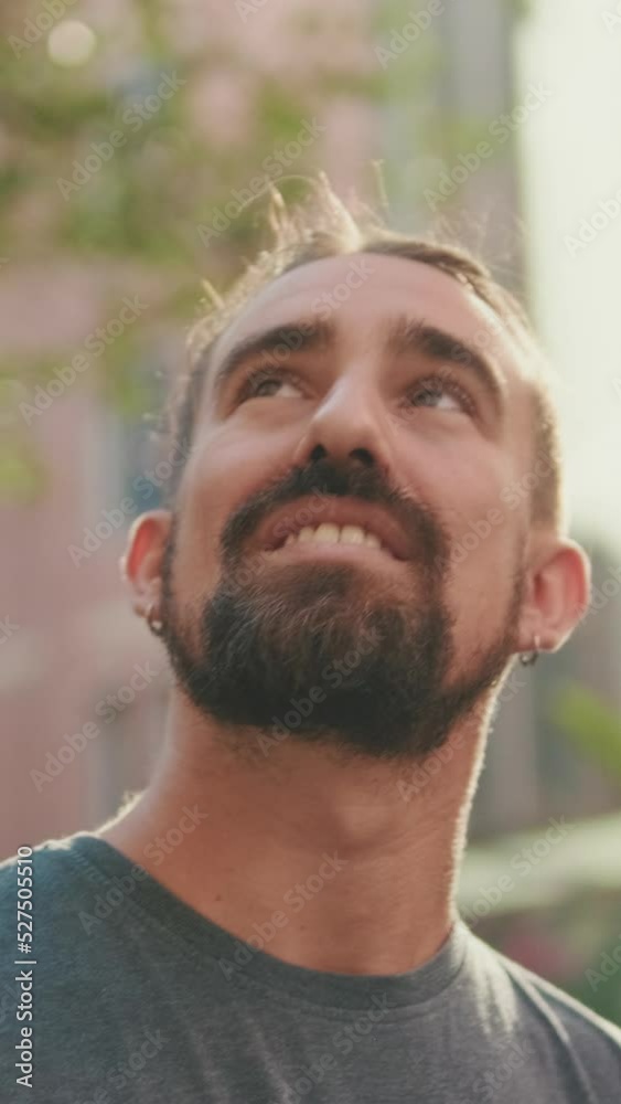VERTICAL VIDEO: Close-up of Young smiling man with beard walking down the street and looking around VERTICAL VIDEO: Close-up of Young smiling man with beard walking down the street and looking around