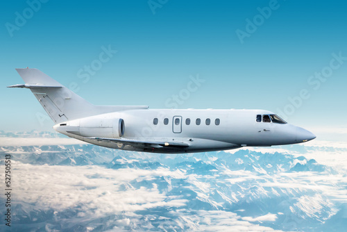 White modern corporate aircraft flies over snow-covered mountains