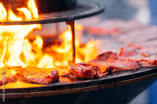 Street food concept. Chef cook prepares Beef steak is fried on open fire outdoor grill in shape of circle
