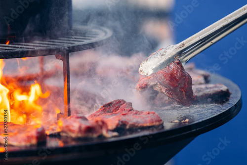 Street food concept. Cook grills steaks and pork ribs open fire. Turns meat over with tongs