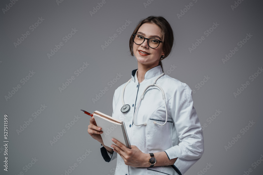 Portrait of doctor woman with notebook and pen dressed in white labcoat isolated on grey. Portrait of doctor woman with notebook and pen dressed in white labcoat isolated on grey.
