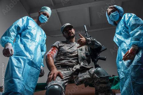 Shot of surgeon and his assistant and military man with rifle looking at camera.