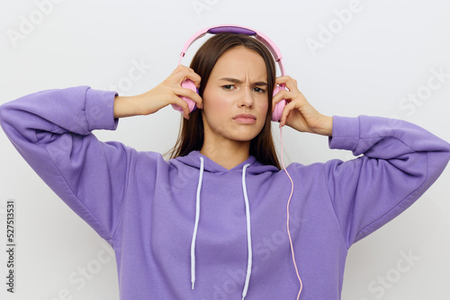 an outraged woman stands on a white background in a purple tracksuit discontentedly putting pink headphones on her ears © Tatiana