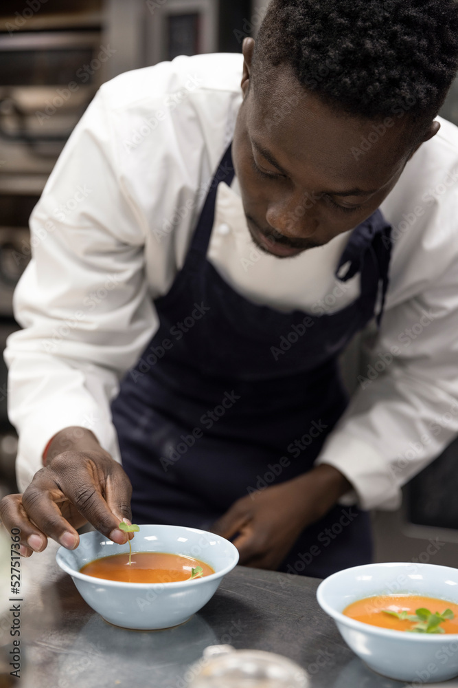 Chef garnishing soup with basil leaves in restaurant kitchen Chef garnishing soup with basil leaves in restaurant kitchen