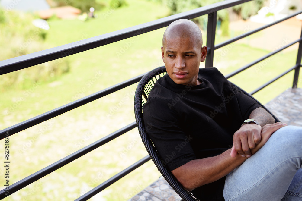 Fototapeta premium Young african american man sitting on armchair on balcony 