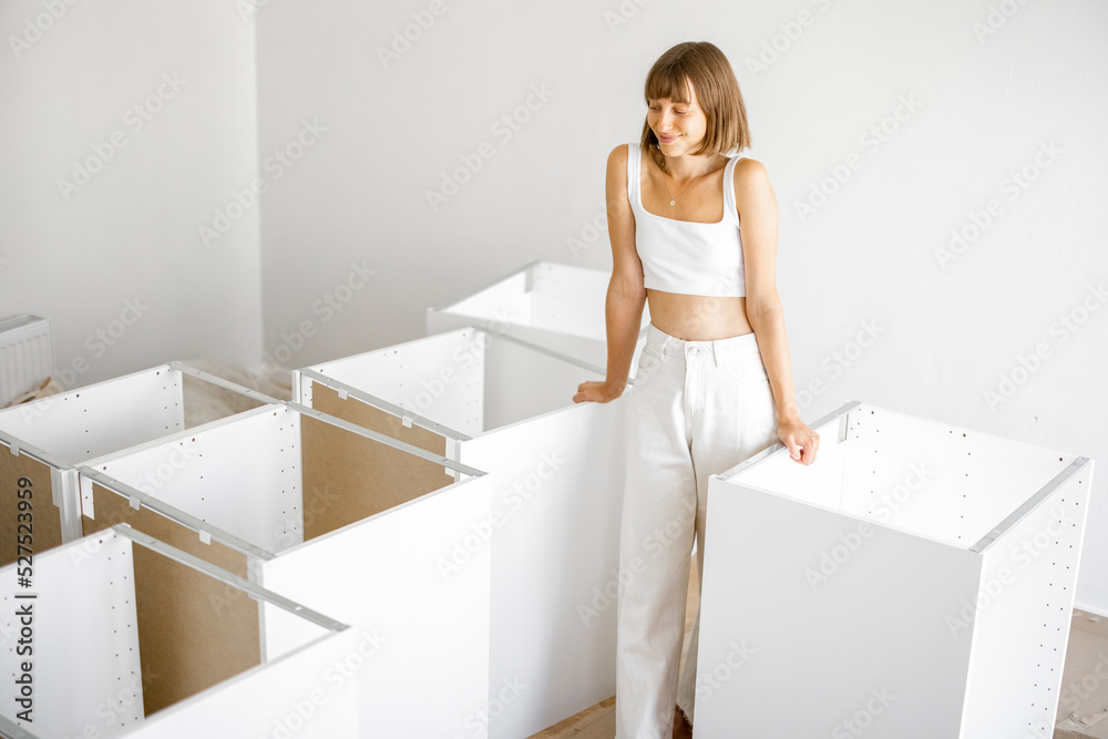 Portrait of a young cheerful housewife stands with new furniture in apartment. Woman in white clothes during home improvement Portrait of a young cheerful housewife stands with new furniture in apartment. Woman in white clothes during home improvement