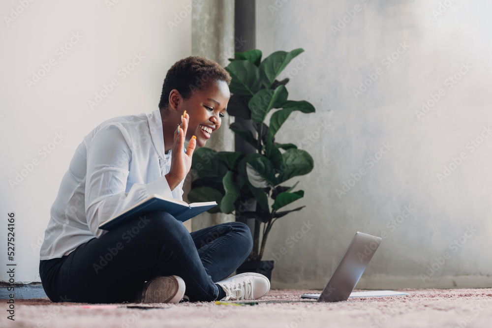 Smiling African American woman sitting at home on the floor, studying ...