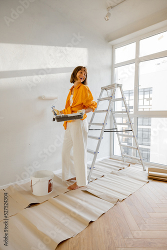 Fotografie Portrait of a young woman making repairing in apartment, standing with paint rol