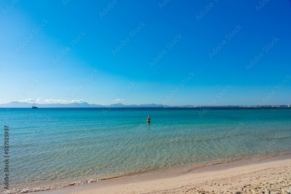 Playa de Alcudia (mallorca): mujer entrando en la tranquilidad de las aguas cristalinas y turquesas de la playa.