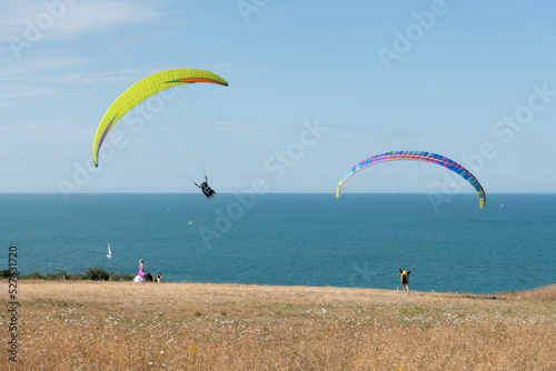 Several paraglider pilots plot a turn overlooking the Atlantic coast with the sea and mountains in the background.