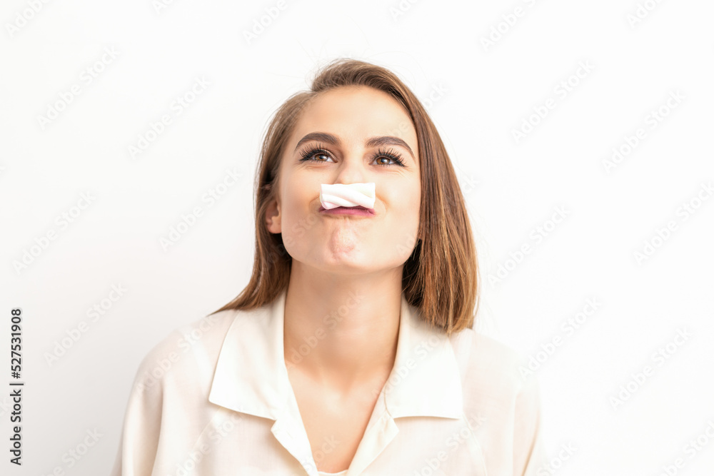 Funny young woman with marshmallow on her lips looking up and standing on white background with copy space Funny young woman with marshmallow on her lips looking up and standing on white background with copy space