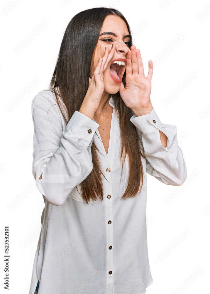 Young beautiful woman wearing casual white shirt shouting angry out loud with hands over mouth Young beautiful woman wearing casual white shirt shouting angry out loud with hands over mouth