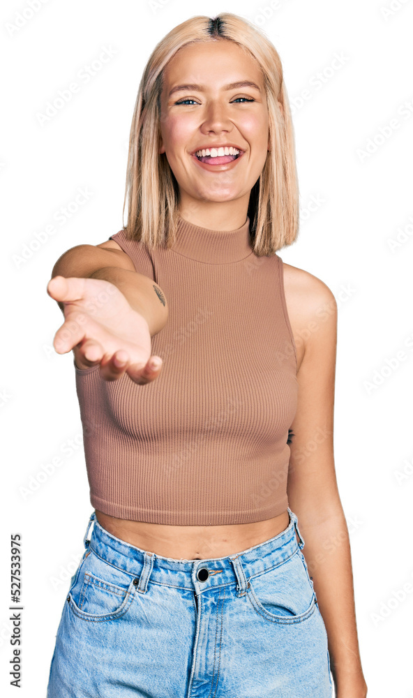 Beautiful young blonde woman offering hand smiling and laughing hard out loud because funny crazy joke. Beautiful young blonde woman offering hand smiling and laughing hard out loud because funny crazy joke.