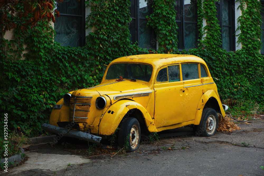 Abandoned old yellow retro car on the old city street.