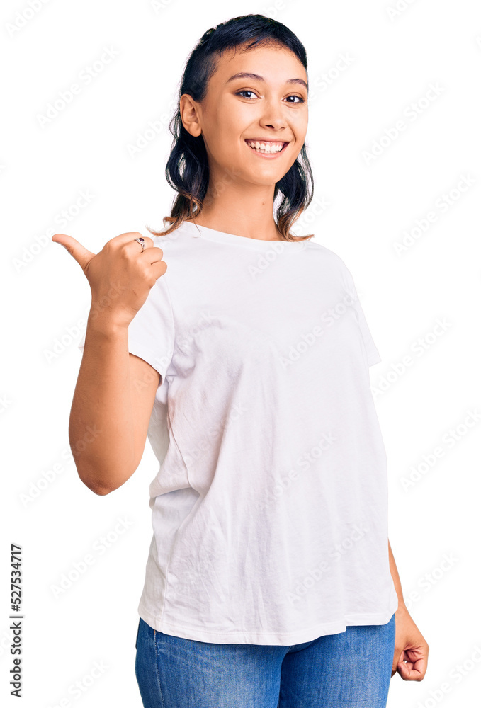 Young woman wearing casual clothes smiling with happy face looking and pointing to the side with thumb up. Young woman wearing casual clothes smiling with happy face looking and pointing to the side with thumb up.
