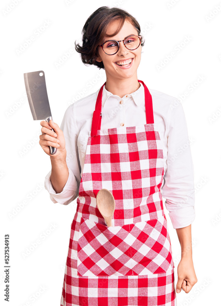 Beautiful young woman with short hair wearing professional baker apron holding knife looking positive and happy standing and smiling with a confident smile showing teeth Beautiful young woman with short hair wearing professional baker apron holding knife looking positive and happy standing and smiling with a confident smile showing teeth