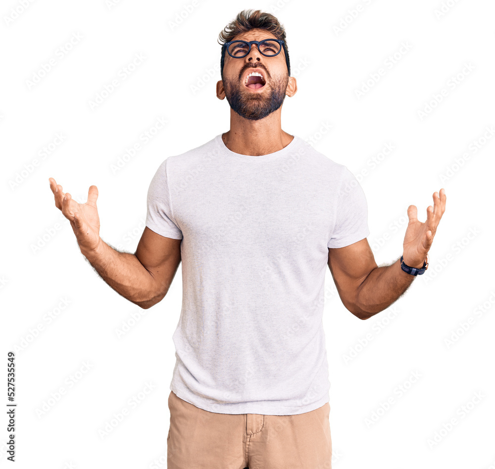 Young hispanic man wearing casual clothes and glasses crazy and mad shouting and yelling with aggressive expression and arms raised. frustration concept. Young hispanic man wearing casual clothes and glasses crazy and mad shouting and yelling with aggressive expression and arms raised. frustration concept.