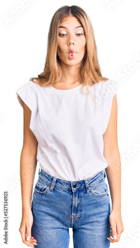 Beautiful caucasian woman with blonde hair wearing casual white tshirt making fish face with lips, crazy and comical gesture. funny expression.