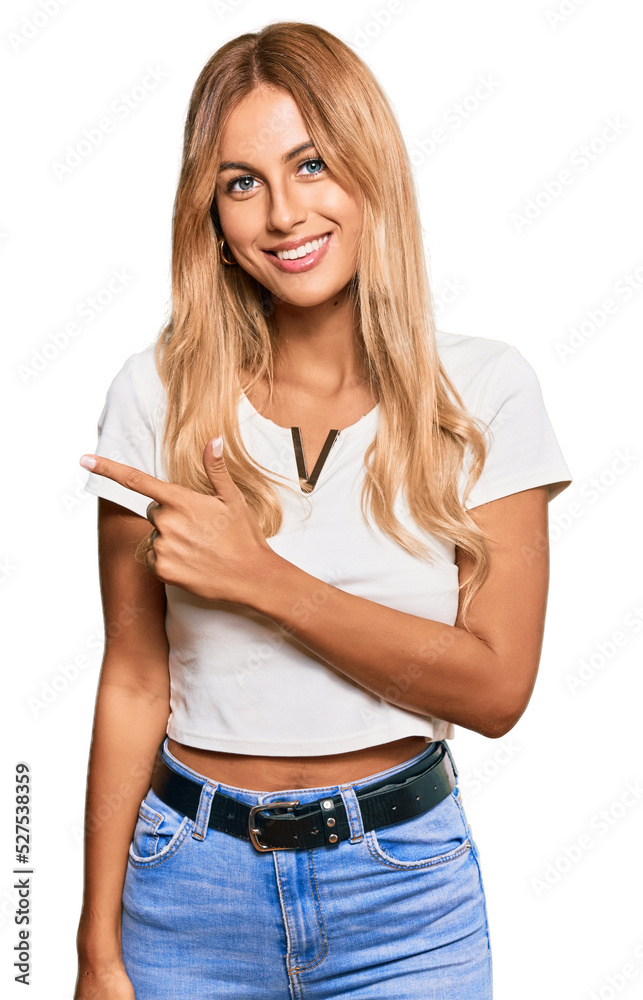 Beautiful blonde young woman wearing casual white tshirt cheerful with a smile of face pointing with hand and finger up to the side with happy and natural expression on face Beautiful blonde young woman wearing casual white tshirt cheerful with a smile of face pointing with hand and finger up to the side with happy and natural expression on face