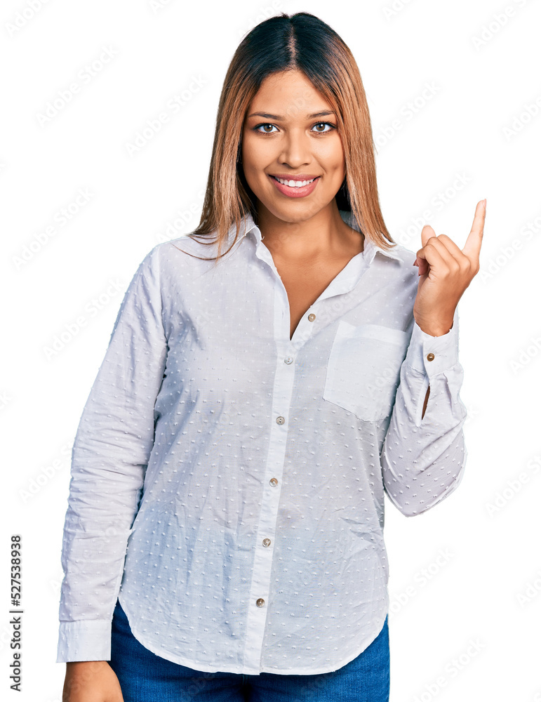Young hispanic woman wearing casual white shirt with a big smile on face, pointing with hand and finger to the side looking at the camera. Young hispanic woman wearing casual white shirt with a big smile on face, pointing with hand and finger to the side looking at the camera.