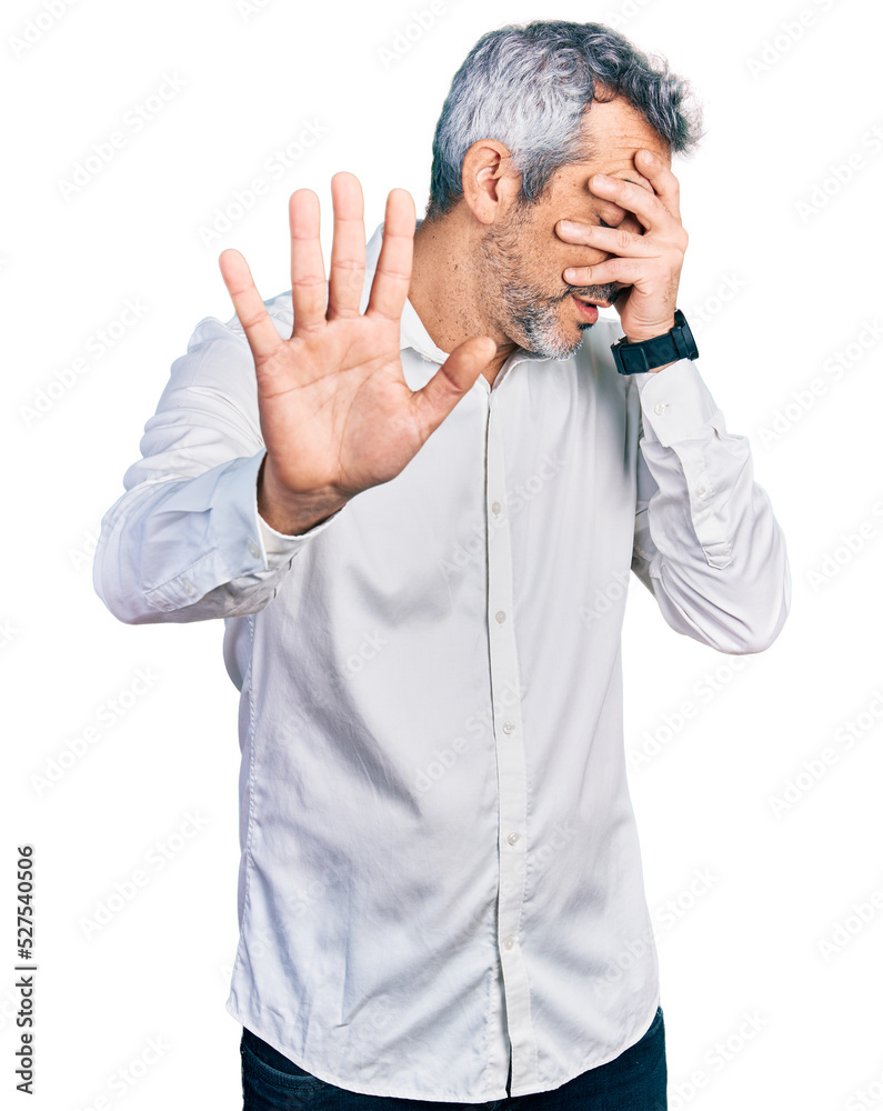 Middle age hispanic with grey hair wearing casual white shirt covering eyes with hands and doing stop gesture with sad and fear expression. embarrassed and negative concept. Middle age hispanic with grey hair wearing casual white shirt covering eyes with hands and doing stop gesture with sad and fear expression. embarrassed and negative concept.