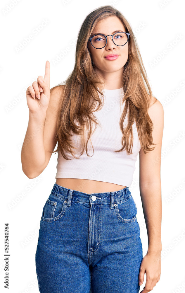 Beautiful caucasian young woman wearing casual clothes and glasses showing and pointing up with finger number one while smiling confident and happy. Beautiful caucasian young woman wearing casual clothes and glasses showing and pointing up with finger number one while smiling confident and happy.