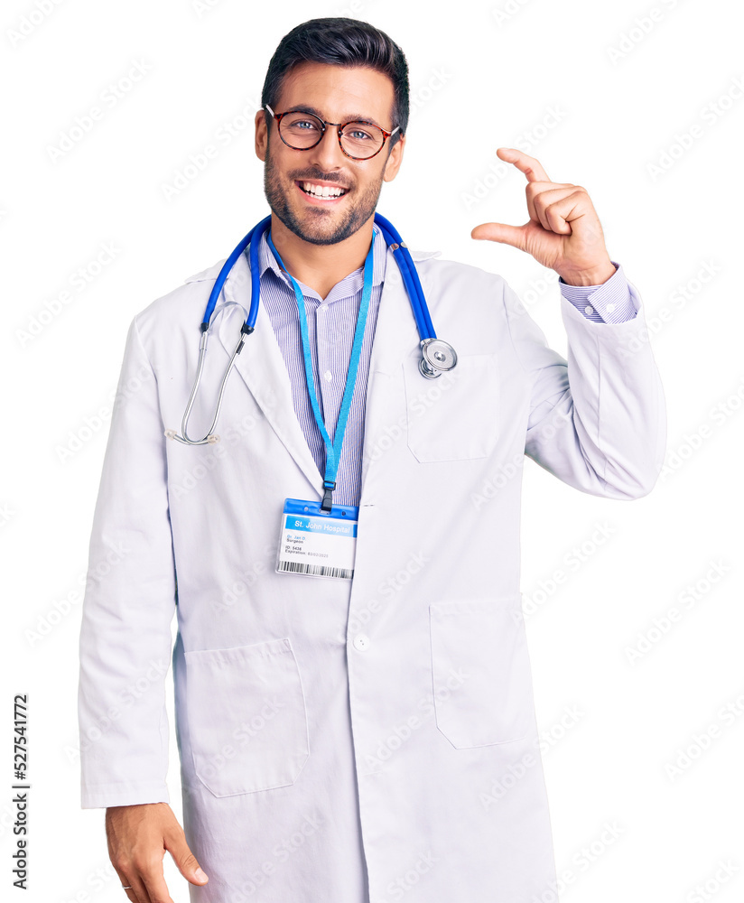 Young hispanic man wearing doctor uniform and stethoscope smiling and confident gesturing with hand doing small size sign with fingers looking and the camera. measure concept. Young hispanic man wearing doctor uniform and stethoscope smiling and confident gesturing with hand doing small size sign with fingers looking and the camera. measure concept.