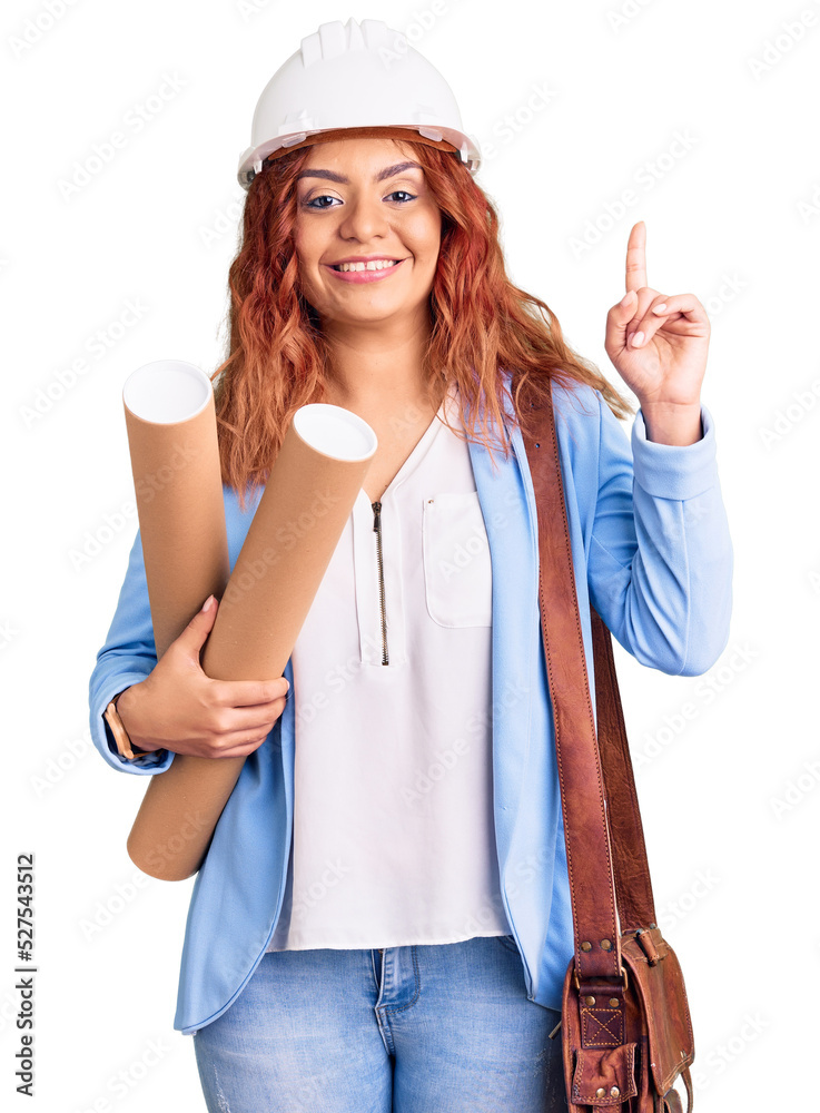 Young latin woman wearing architect hardhat holding blueprints surprised with an idea or question pointing finger with happy face, number one Young latin woman wearing architect hardhat holding blueprints surprised with an idea or question pointing finger with happy face, number one