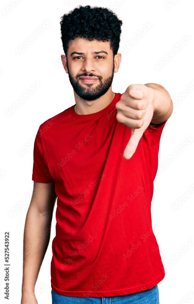 Young arab man with beard wearing casual red t shirt looking unhappy and angry showing rejection and negative with thumbs down gesture. bad expression. Young arab man with beard wearing casual red t shirt looking unhappy and angry showing rejection and negative with thumbs down gesture. bad expression.