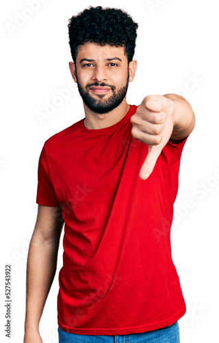 Young arab man with beard wearing casual red t shirt looking unhappy and angry showing rejection and negative with thumbs down gesture. bad expression.