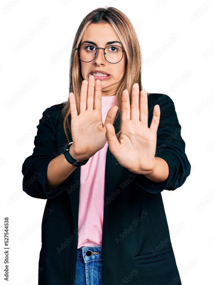 Hispanic young woman wearing business jacket and glasses afraid and terrified with fear expression stop gesture with hands, shouting in shock. panic concept.