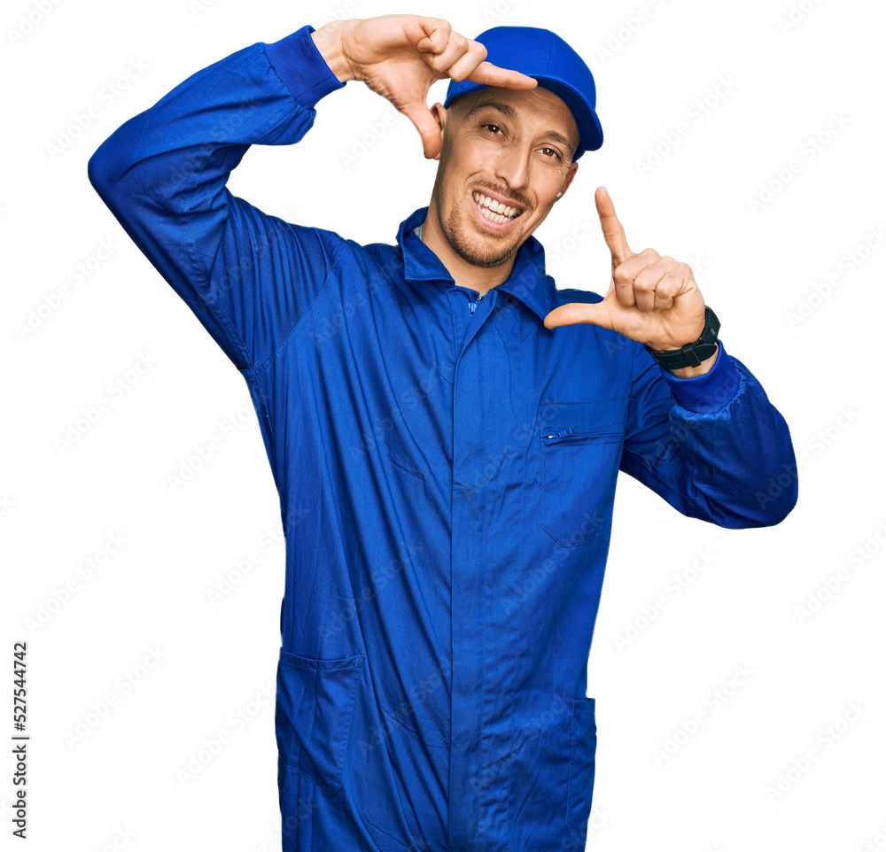 Bald man with beard wearing builder jumpsuit uniform smiling making frame with hands and fingers with happy face. creativity and photography concept.