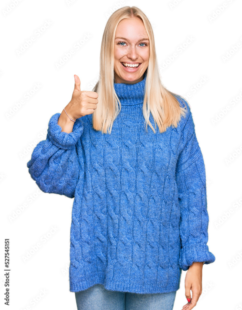 Young blonde girl wearing wool winter sweater smiling happy and positive, thumb up doing excellent and approval sign Young blonde girl wearing wool winter sweater smiling happy and positive, thumb up doing excellent and approval sign