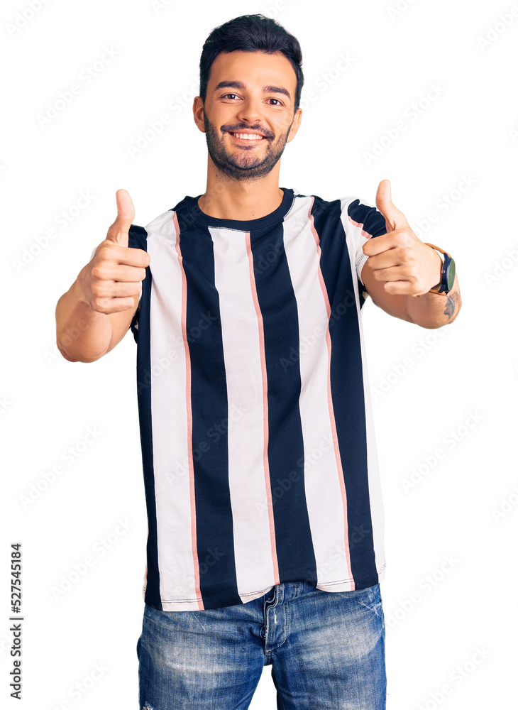 Fototapeta premium Young handsome hispanic man wearing striped tshirt approving doing positive gesture with hand, thumbs up smiling and happy for success. winner gesture.