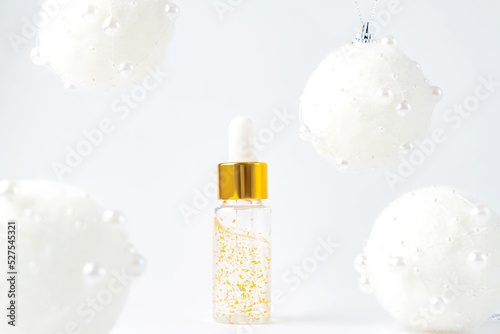 bottle of 24k gold serum on a white background with christmas baubles around. The concept of skin care presents for new year holidays. photo