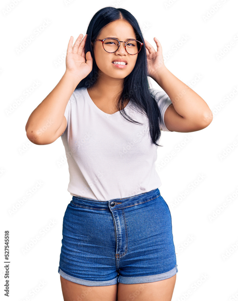 Young beautiful asian girl wearing casual clothes and glasses trying to hear both hands on ear gesture, curious for gossip. hearing problem, deaf Young beautiful asian girl wearing casual clothes and glasses trying to hear both hands on ear gesture, curious for gossip. hearing problem, deaf