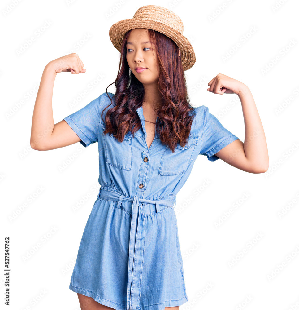 Young beautiful chinese girl wearing summer hat showing arms muscles smiling proud. fitness concept. Young beautiful chinese girl wearing summer hat showing arms muscles smiling proud. fitness concept.