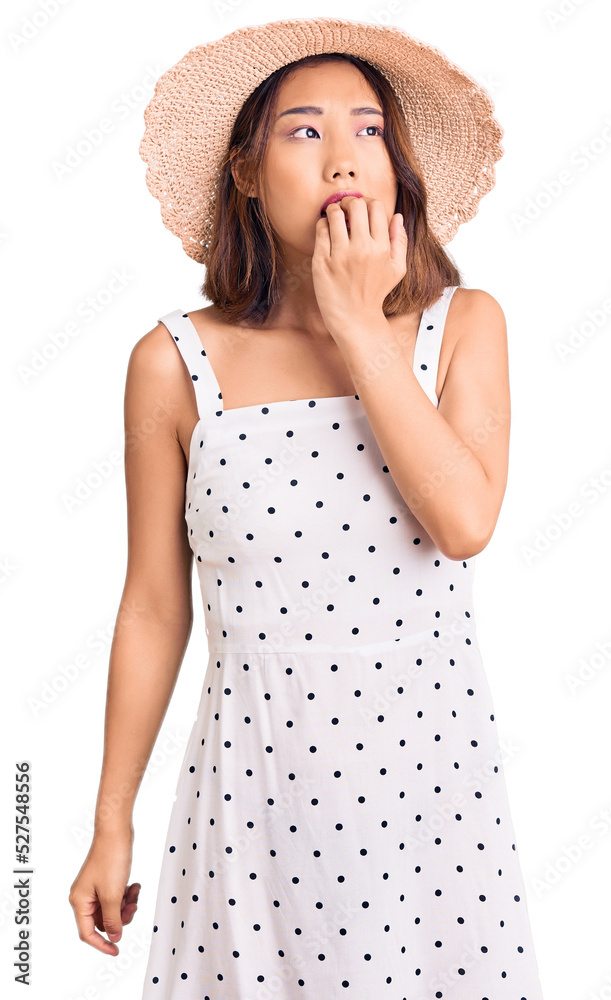 Young beautiful chinese girl wearing summer hat looking stressed and nervous with hands on mouth biting nails. anxiety problem. Young beautiful chinese girl wearing summer hat looking stressed and nervous with hands on mouth biting nails. anxiety problem.