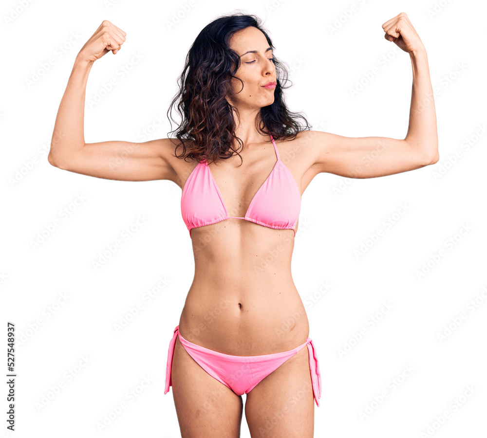 Young beautiful hispanic woman wearing bikini showing arms muscles smiling proud. fitness concept. Young beautiful hispanic woman wearing bikini showing arms muscles smiling proud. fitness concept.