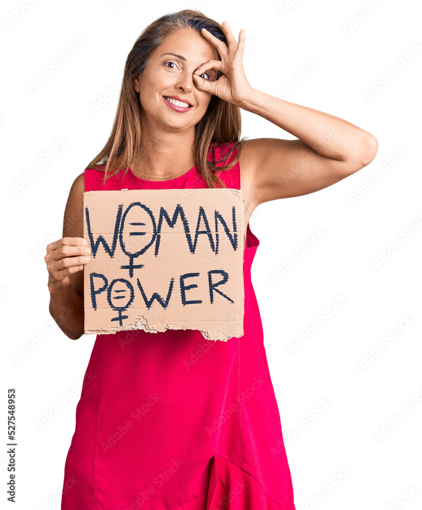 Middle age hispanic woman holding woman power banner smiling happy doing ok sign with hand on eye looking through fingers Middle age hispanic woman holding woman power banner smiling happy doing ok sign with hand on eye looking through fingers