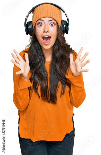 Beautiful brunette young woman listening to music using headphones celebrating crazy and amazed for success with arms raised and open eyes screaming excited. winner concept