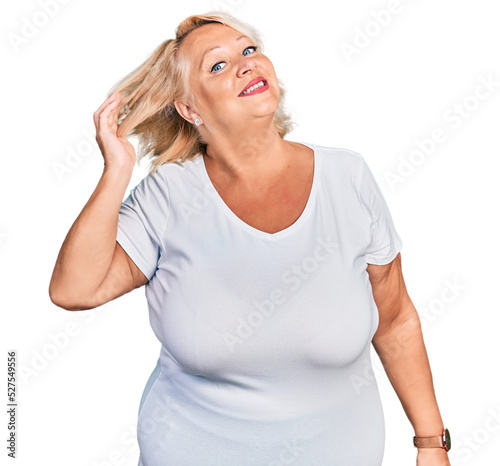 Middle age blonde woman wearing casual white t shirt smiling confident touching hair with hand up gesture, posing attractive and fashionable