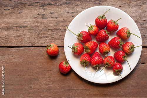 Strawberries on a white ceramic plate and placed on a wooden floor, top view.