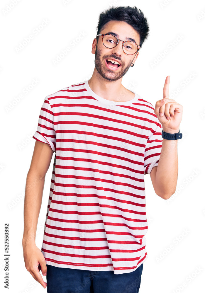 Young hispanic man wearing casual clothes pointing finger up with successful idea. exited and happy. number one. Young hispanic man wearing casual clothes pointing finger up with successful idea. exited and happy. number one.