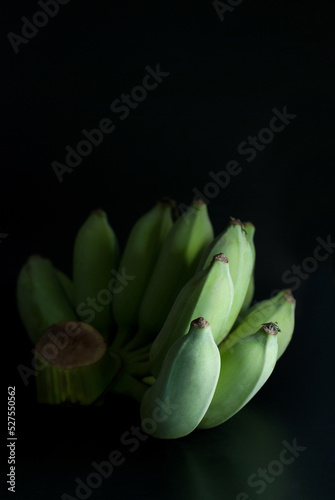 Green raw bananas are placed on a black background.