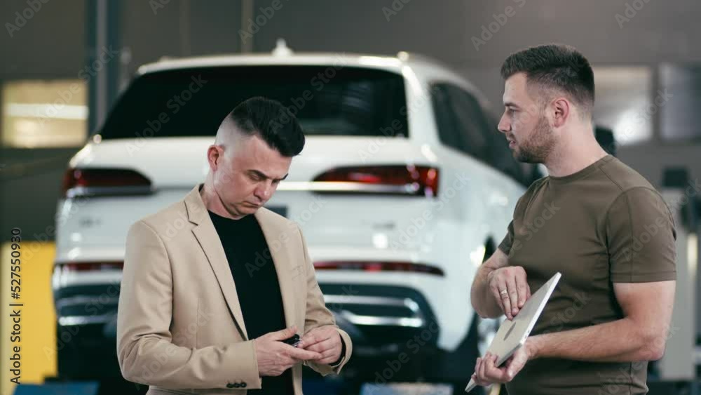 service station, a young professional man shows a satisfied client on a tablet the technical condition of the car, smiles and gives the keys to the car service station, a young professional man shows a satisfied client on a tablet the technical condition of the car, smiles and gives the keys to the car