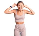 Beautiful caucasian woman wearing sportswear smiling pulling ears with fingers, funny gesture. audition problem