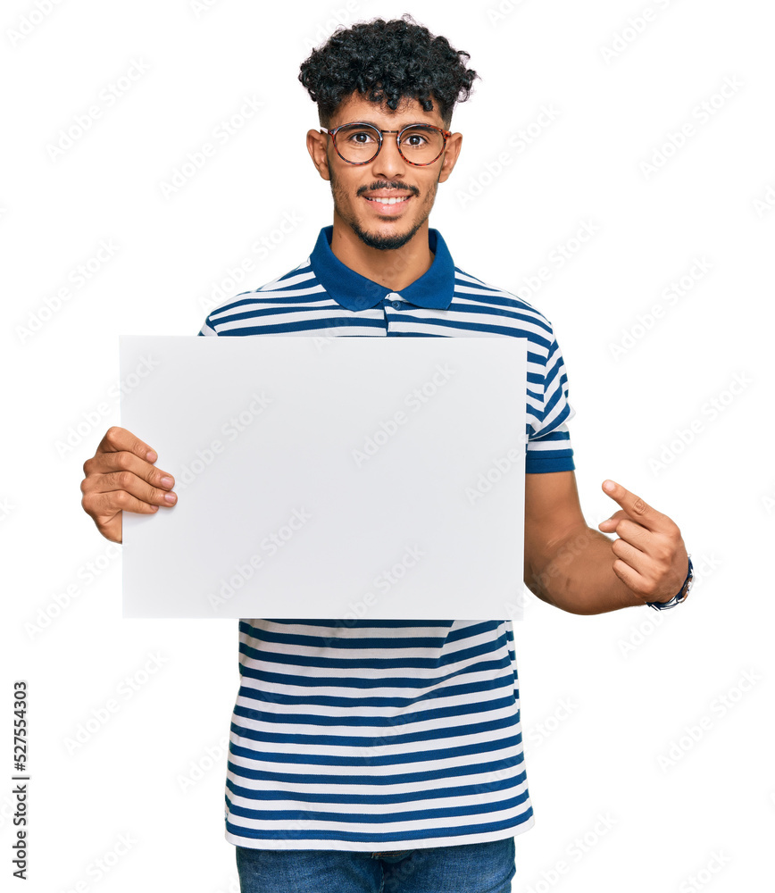 Young arab man holding blank empty banner smiling happy pointing with hand and finger Young arab man holding blank empty banner smiling happy pointing with hand and finger